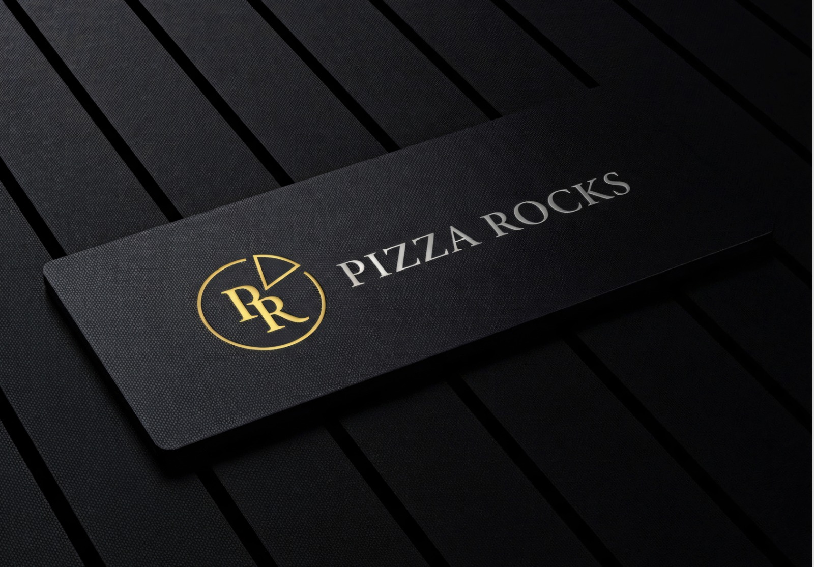 Pizza Rocks embossed black presentation card with gold monogram on a ribbed black surface